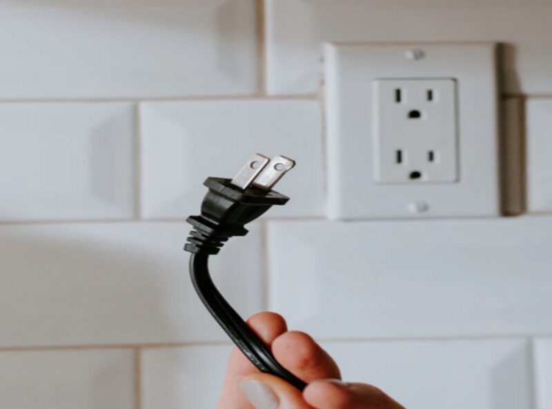 A person holding an electric wire near the electric socket